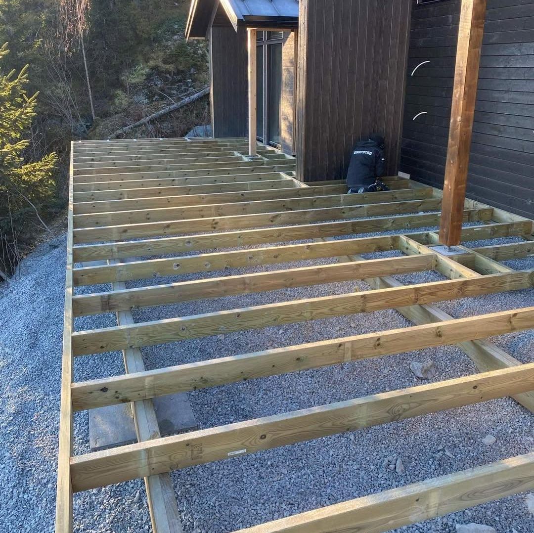 Ansatt hos Brødrene Hofstad AS bygger terrasse ved hytte.